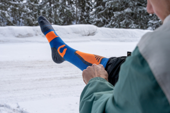 Man trekt zijn skisokken aan in een besneeuwd landschap