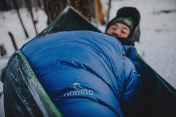Man in dikke, blauwe NOMAD slaapzak in de sneeuw