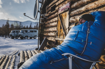 Man in dikke, blauwe NOMAD slaapzak in de sneeuw