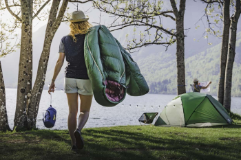 Kampeerster loopt met groene NOMAD slaapzak over de schouder naar haar tent