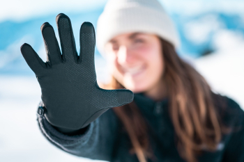 Een vrouw in een zonnige, besneeuwde omgeving met NOMAD handschoenen aan