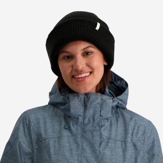 NOMAD Turoa Beanie women’s black knitted hat with logo worn by a woman in a blue outdoor jacket