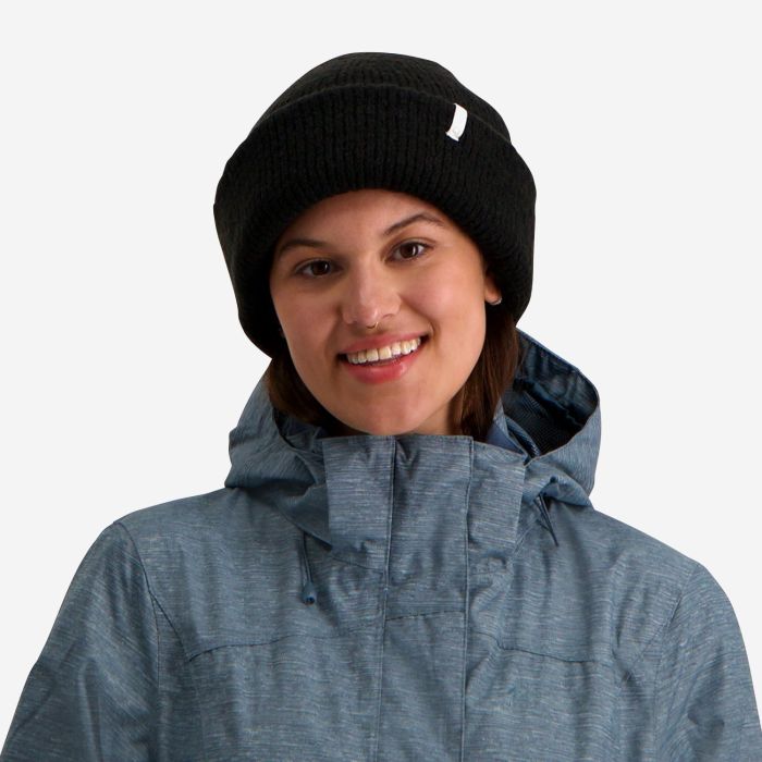 NOMAD Turoa Beanie dames zwart gebreide muts met logo gedragen door vrouw met blauwe outdoorjas
