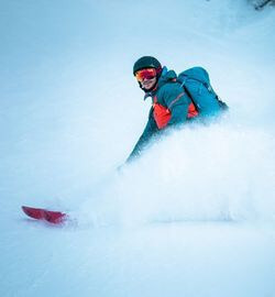 Een wintersporter in actie op een besneeuwde berghelling, uitgerust met technische wintersportkleding en accessoires van NOMAD.