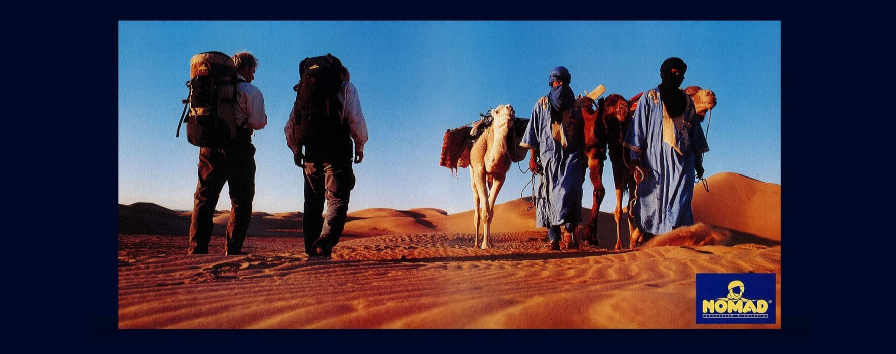 two backpackers in the desert with camels