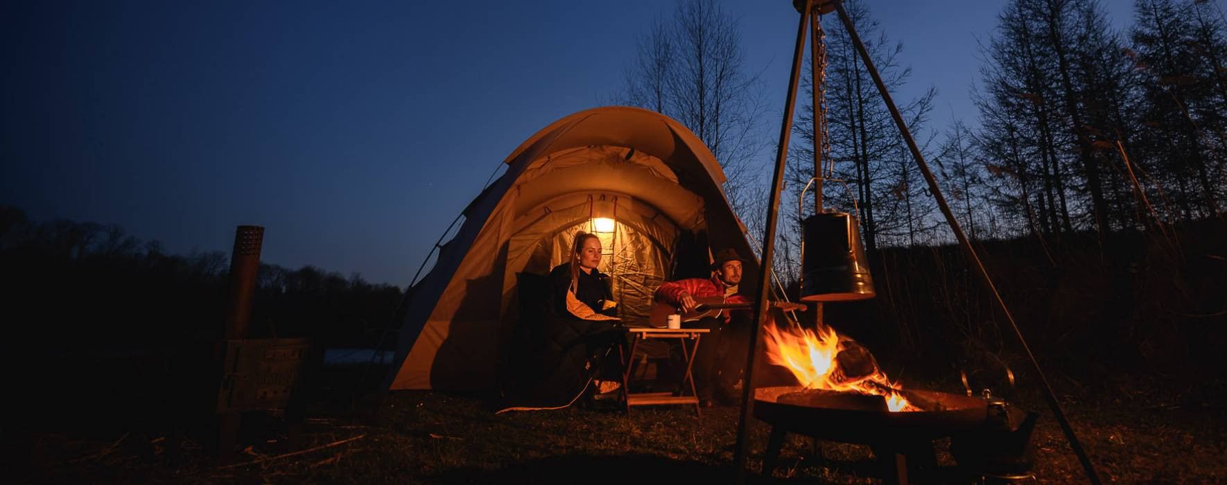Koppel in de avond bij een kampvuur in hun tent waar ze muziek spelen.