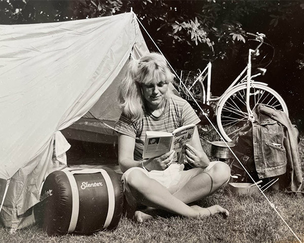 black and white photo of girl sitting in front of tent with a book