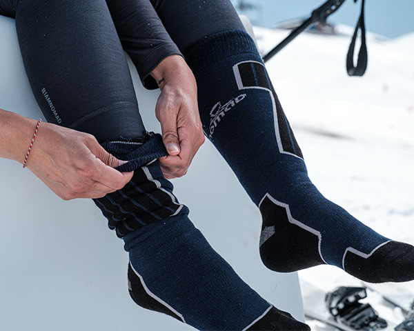 Een paar handen die skisokken op een stoel in de sneeuw aantrekken